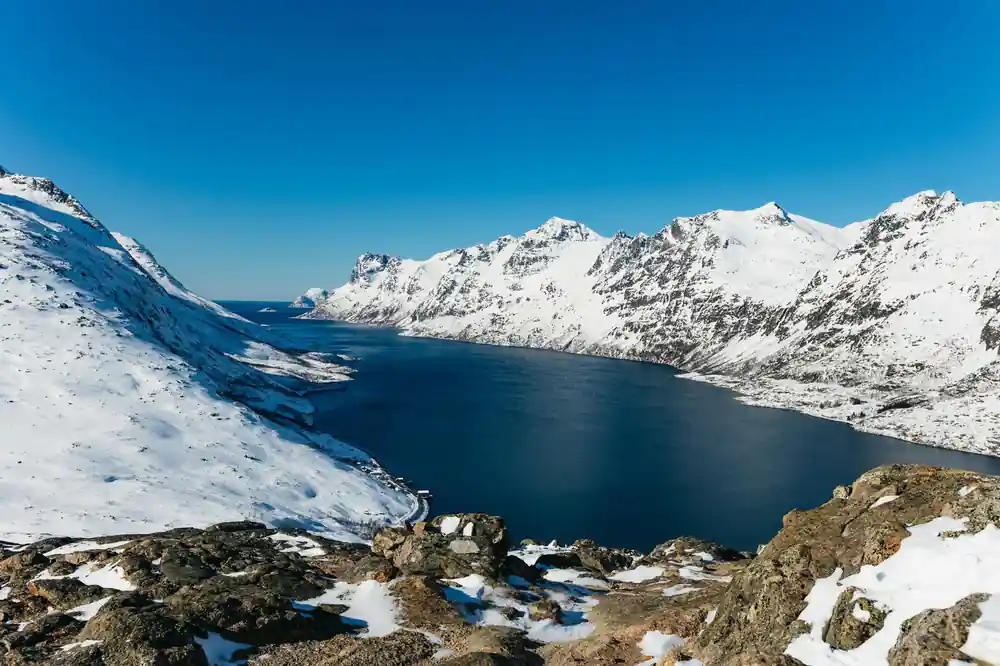 A fjord of dark water below snow-covered mountains