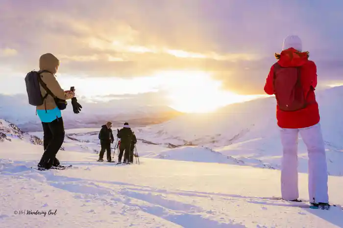 The winter sun low over the snow with figures watching